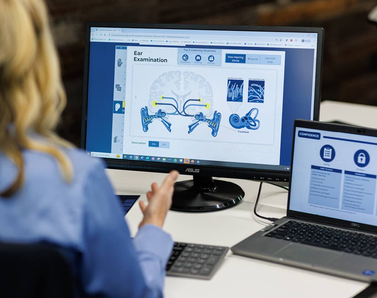 A woman looking at a computer with an image of how hearing works on the screen.