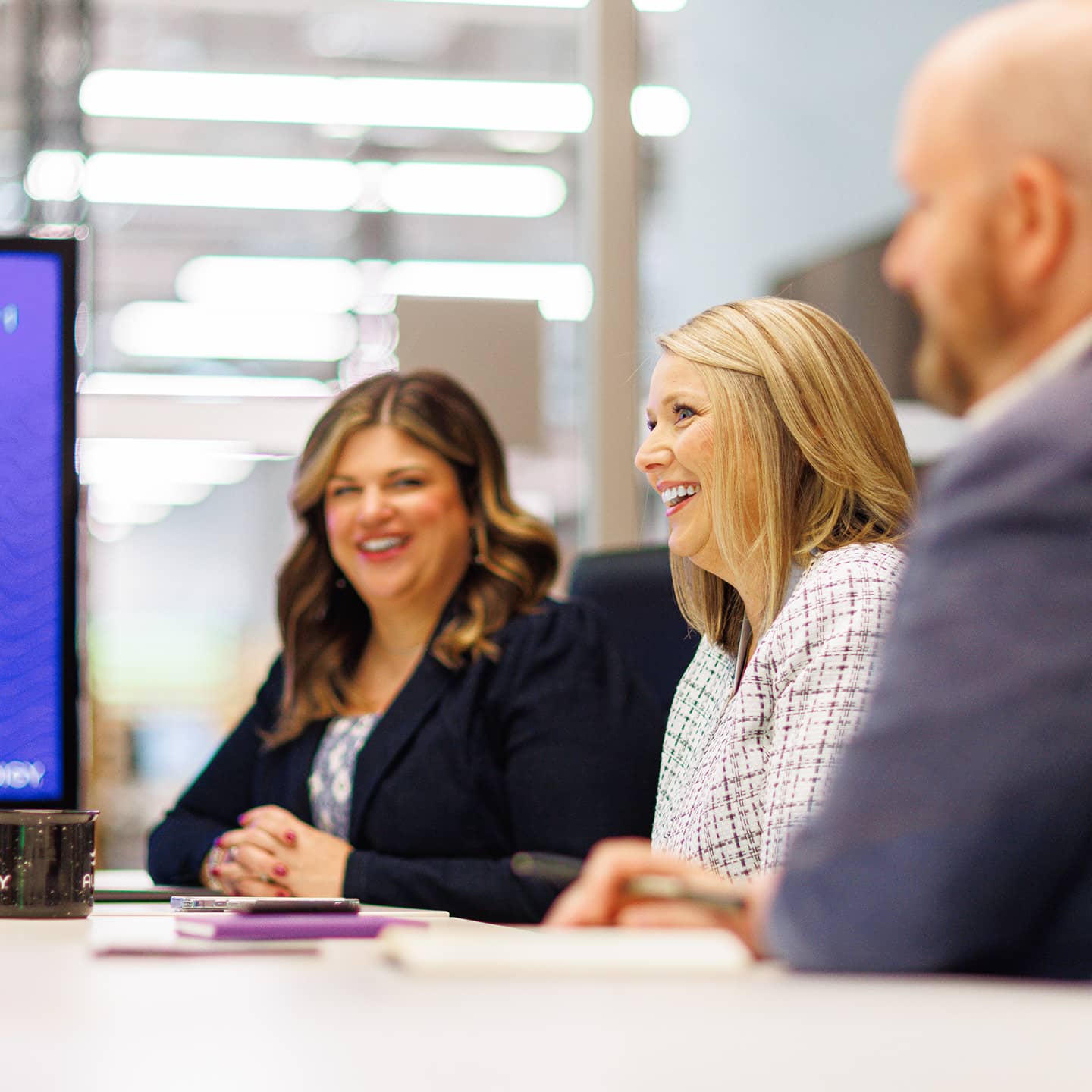 Three professionals meeting in front of a television with graphs on it