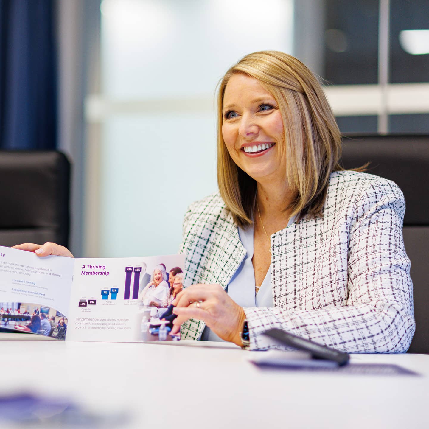 A female professional sitting at a table showing someone off-screen a piece of marketing collateral.