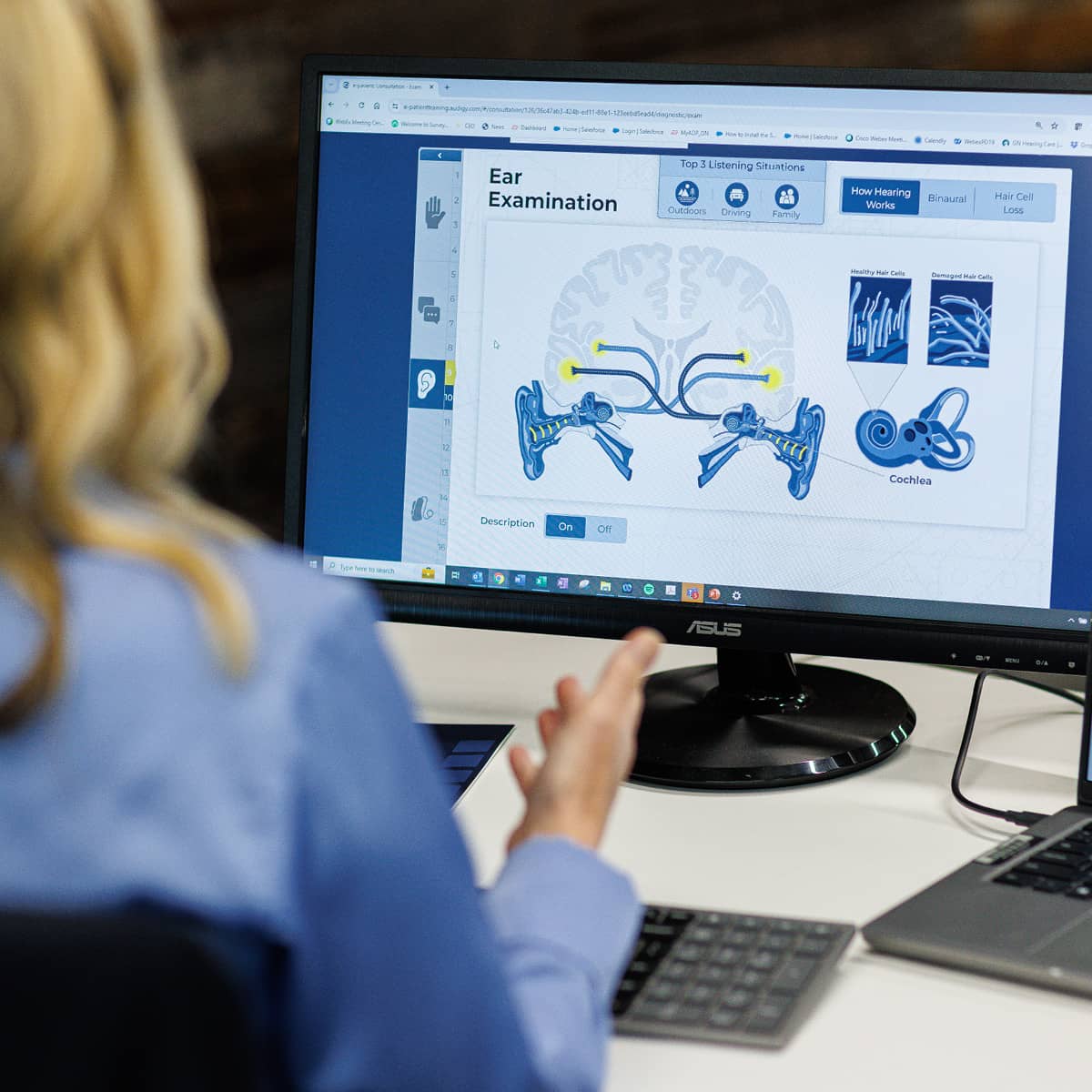 A woman looking at a computer with an image of how hearing works on the screen.