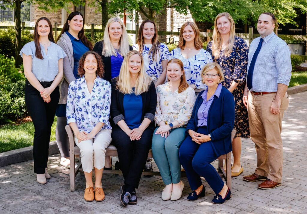 a team of hearing care professionals in a group photo, with some sitting and some standing behind them.