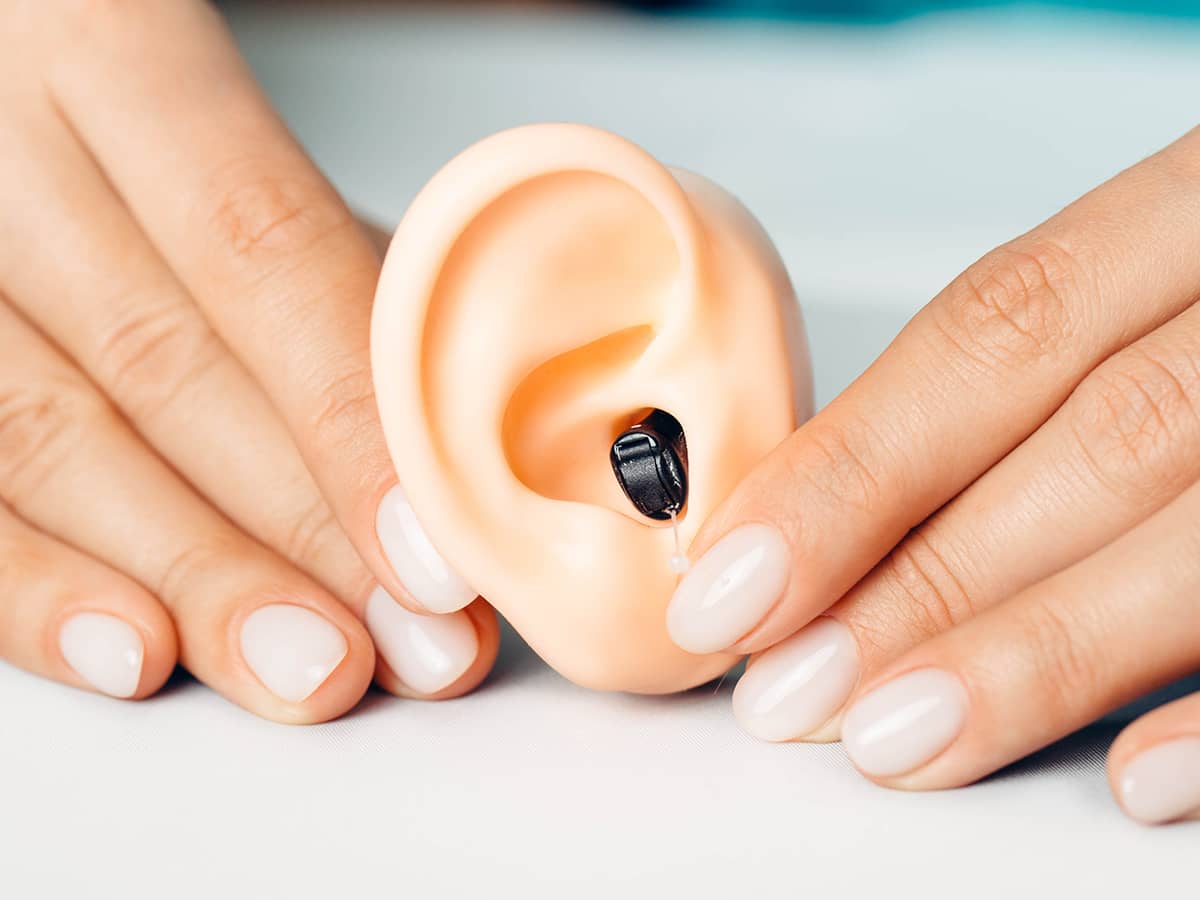 A professional holding a synthetic ear and hearing aid.