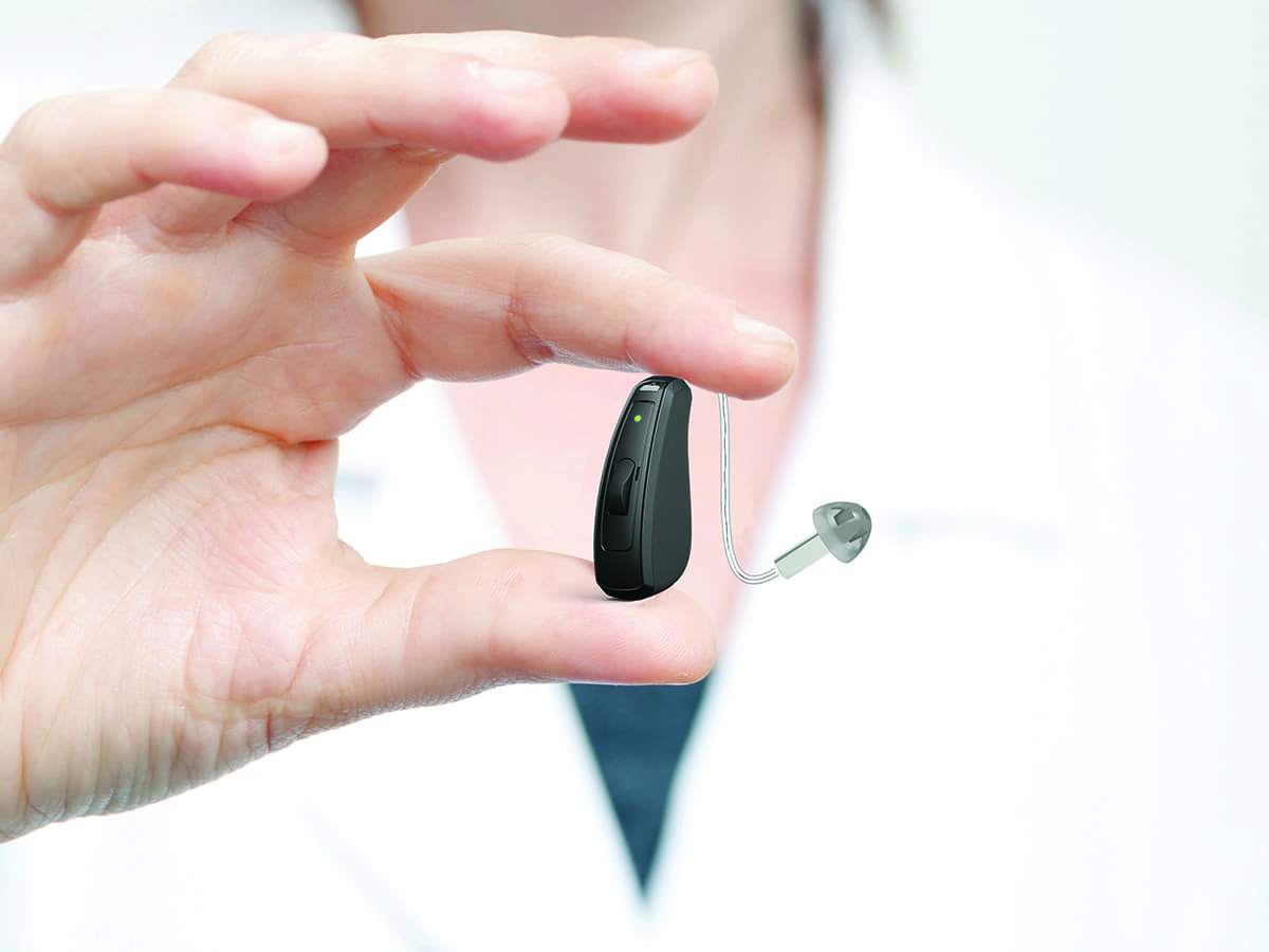 A female professional holding a hearing aid up close.