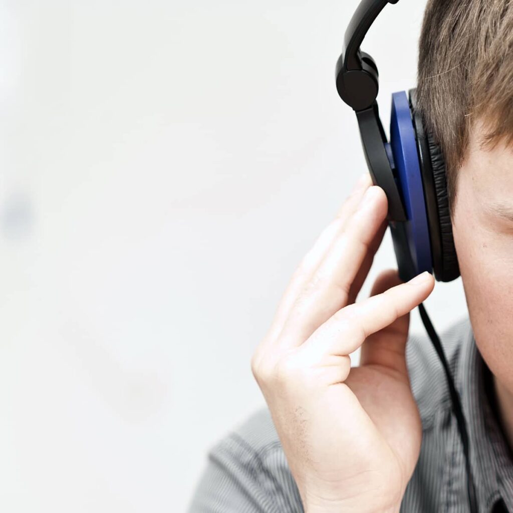 The right side of a male patient's head, wearing audiology evaluation headphones, holding the right side with his hand.