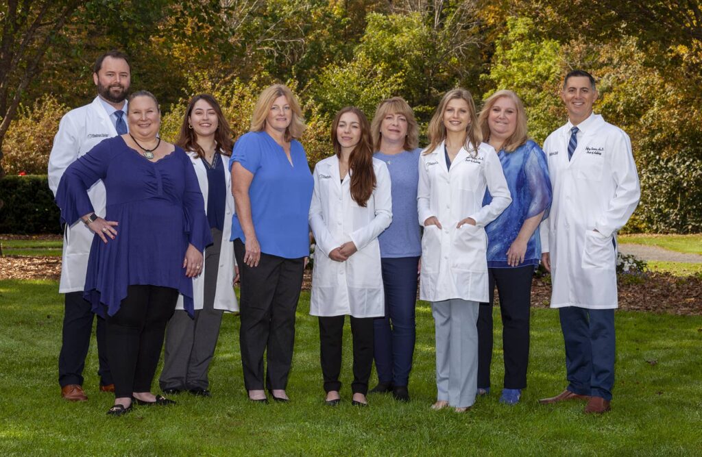 a team of hearing care professionals gathered for a team picture outdoors, all smiling at the viewer.