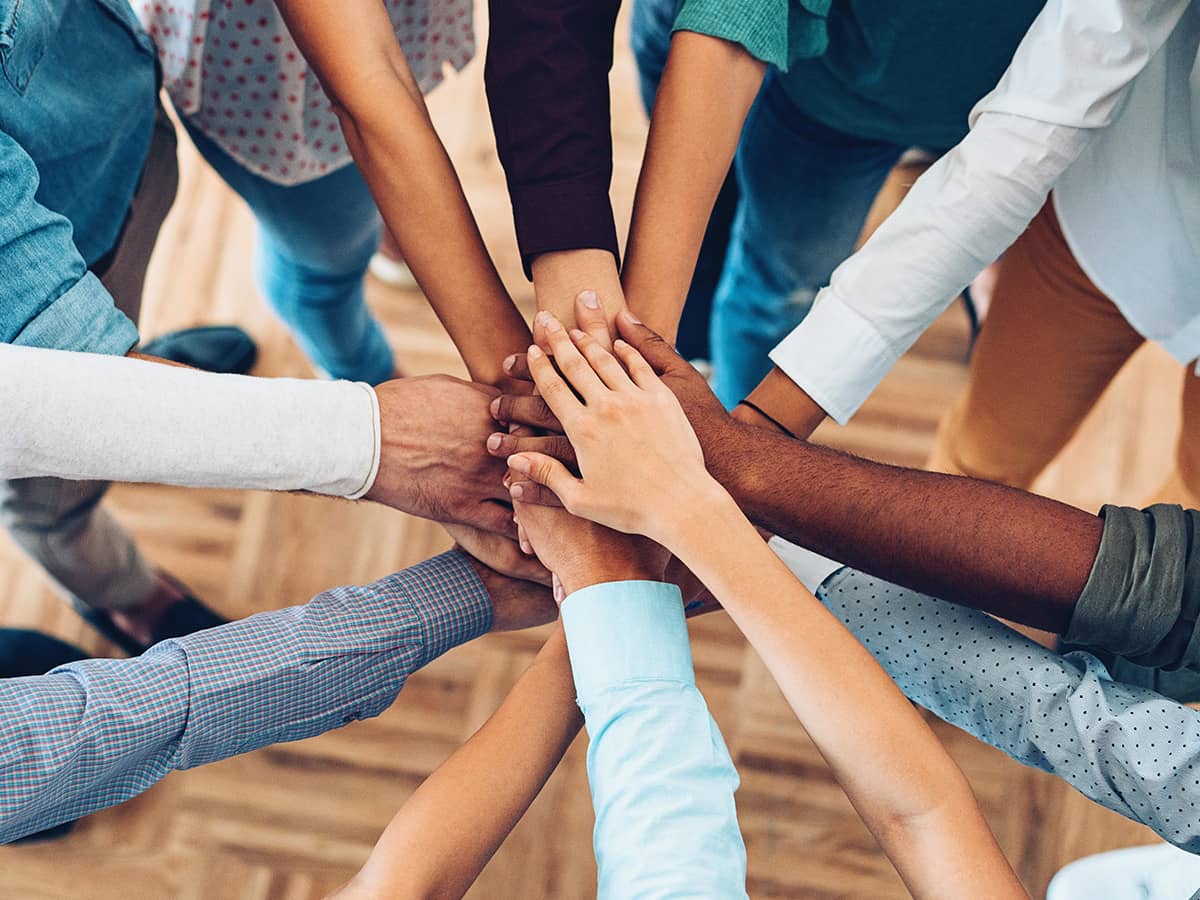 A team of people with their hands together, standing in a circle.